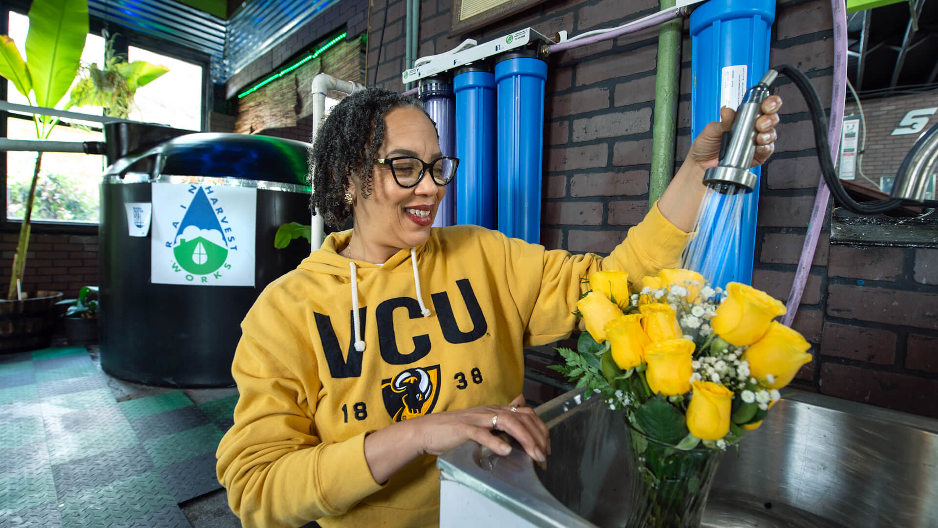 A woman in a VCU sweatshirt adds water to a vase of roses.