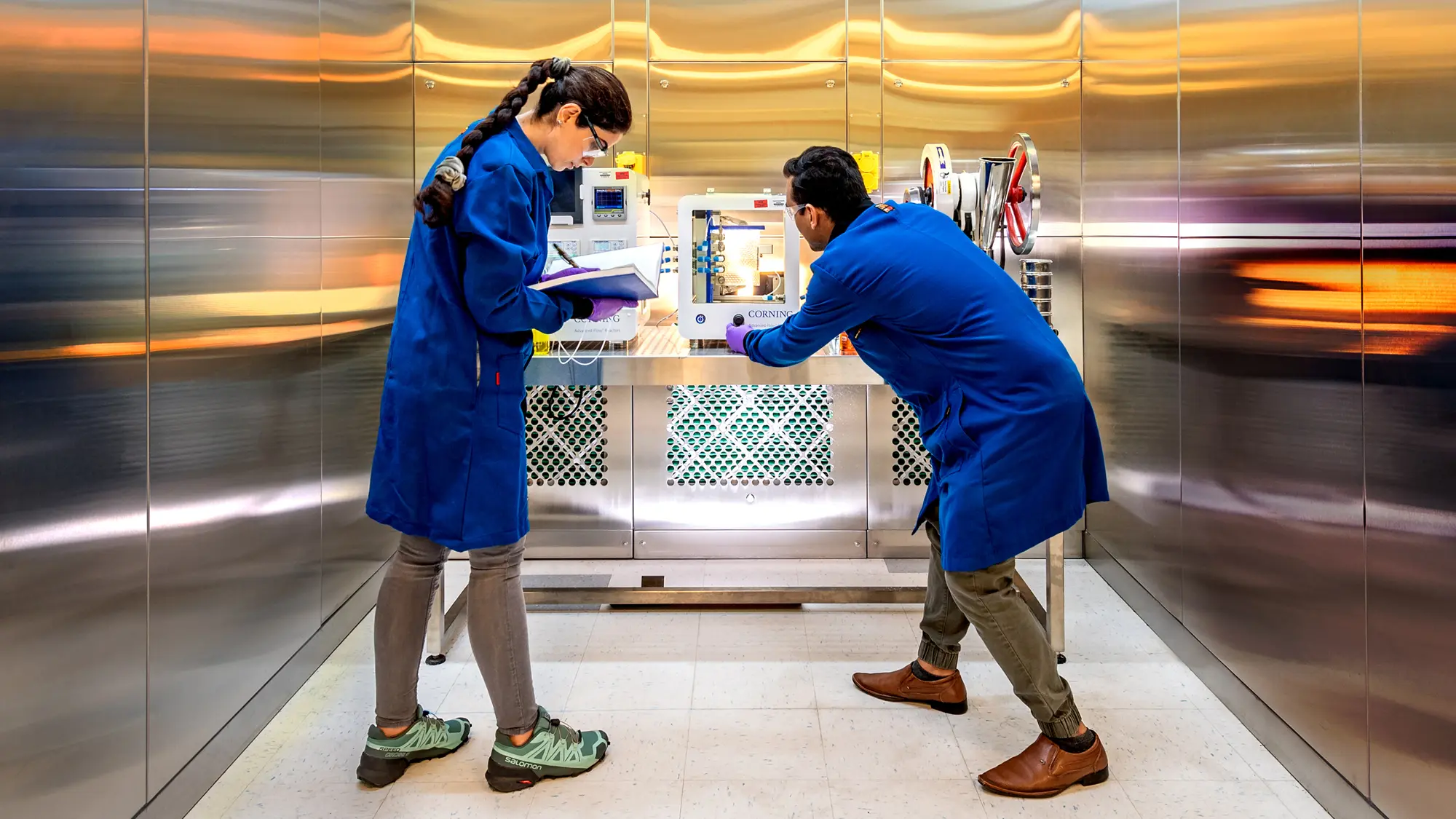 Two students wearing blue lab coats as they work in a VCU laboratory