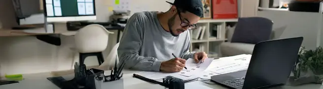 A student sitting at a large desk taking notes on a notepad while taking an online writing course offered by VCU Online